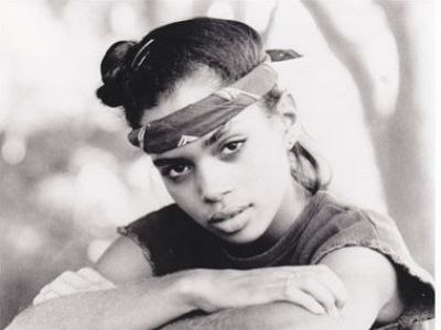 Lisa Bonet is posing with her hands folded and has tied a handkerchief around her forehead.